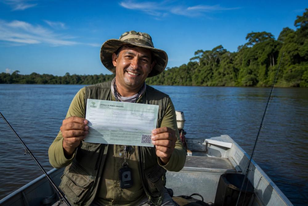 Pescador em barco na Amazônia segurando documento de licença de pesca amadora válida