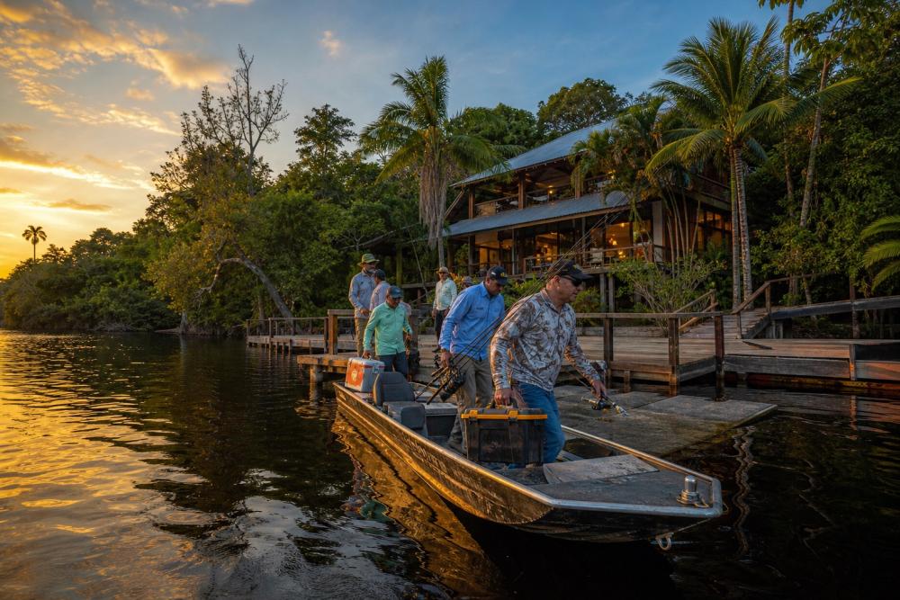 Pescadores chegando de barco a um lodge de pesca na Amazônia durante o pôr do sol
