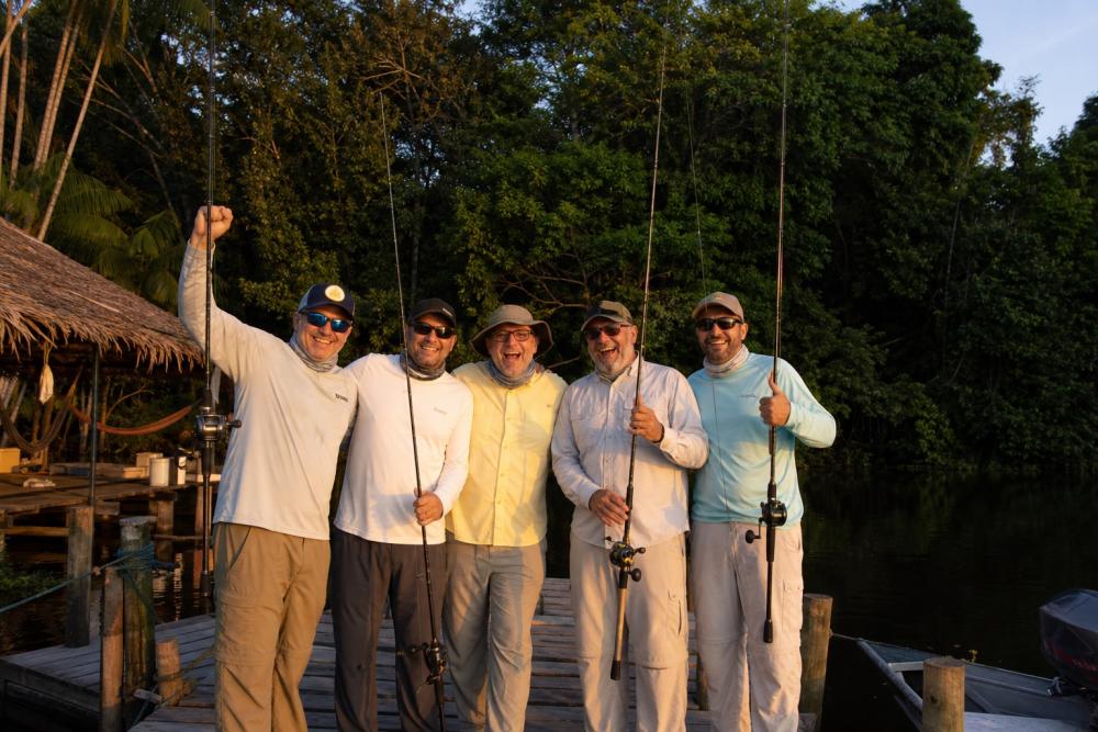 Grupo de pescadores esportivos reunidos em deck de lodge na Amazônia durante o pôr do sol